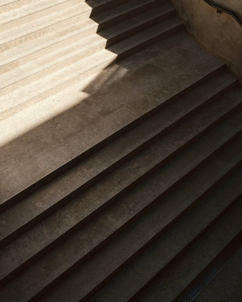 Soft daylight falls across a concrete staircase, each step defined by light and shadow.